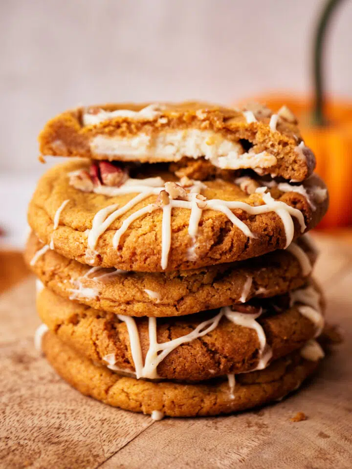 Stack of pumpkin cheesecake cookies, top one cut in half to reveal cheesecake filling.