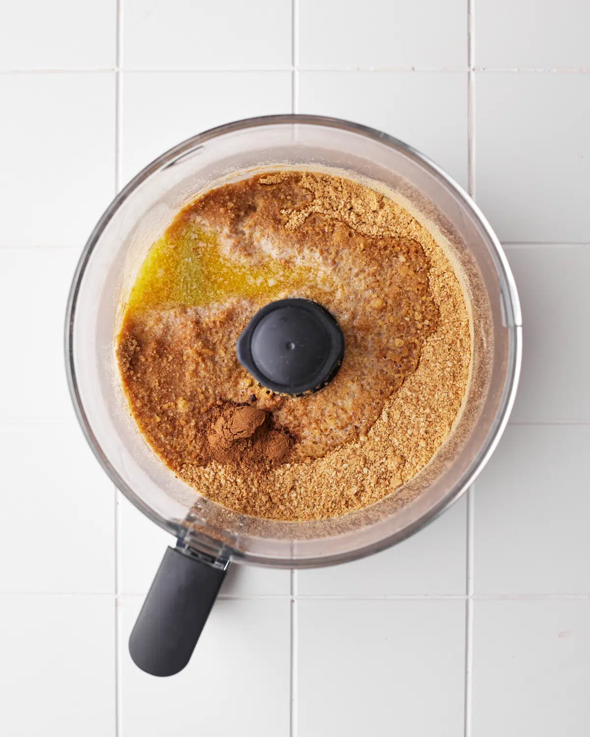 graham cracker crumbs and butter in a food processor ready to be mixed.