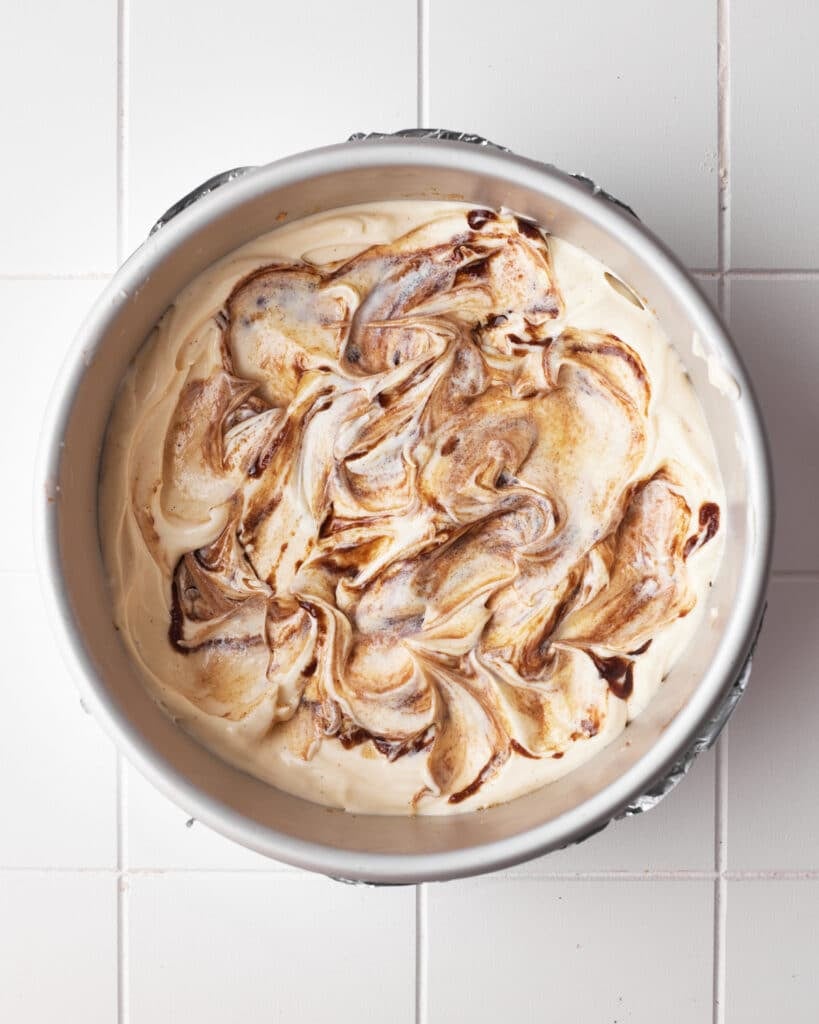 cinnamon filling being swirled into the center of cinnamon roll cheesecake.