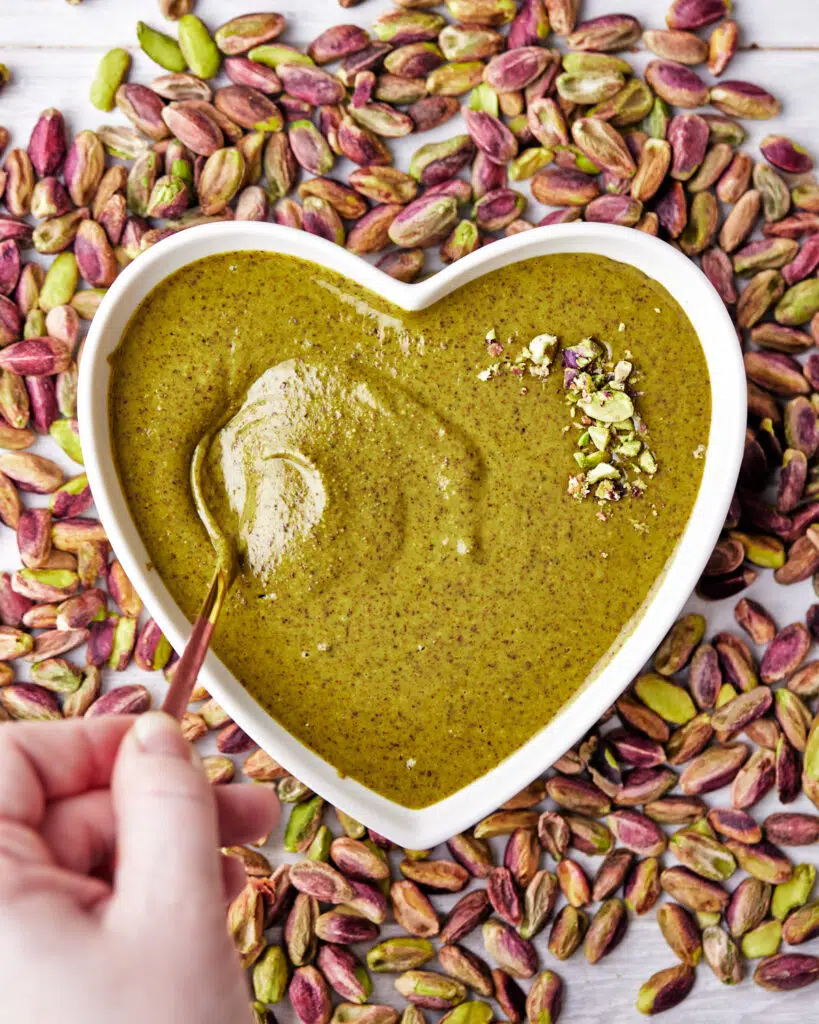 scooping a spoonful of pistachio butter in a heart shaped bowl.