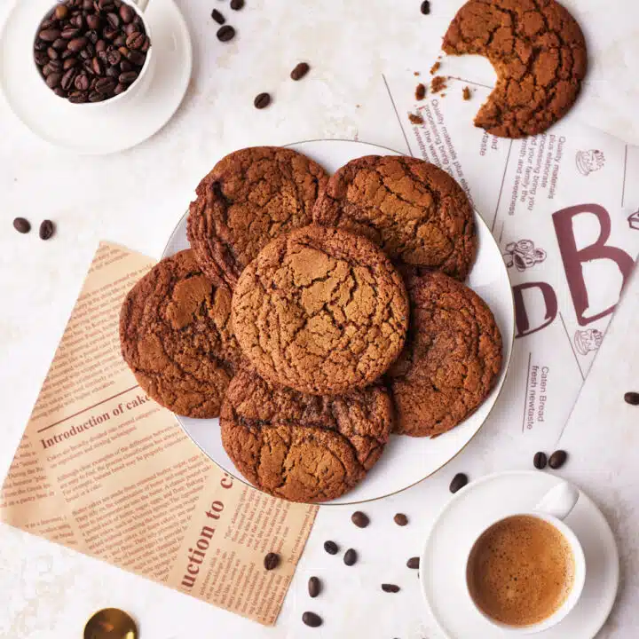 coffee cookies in a pile on a plate, surrounded by coffee beans and espresso.