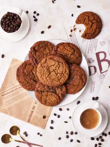 coffee cookies in a pile on a plate, surrounded by coffee beans and espresso.