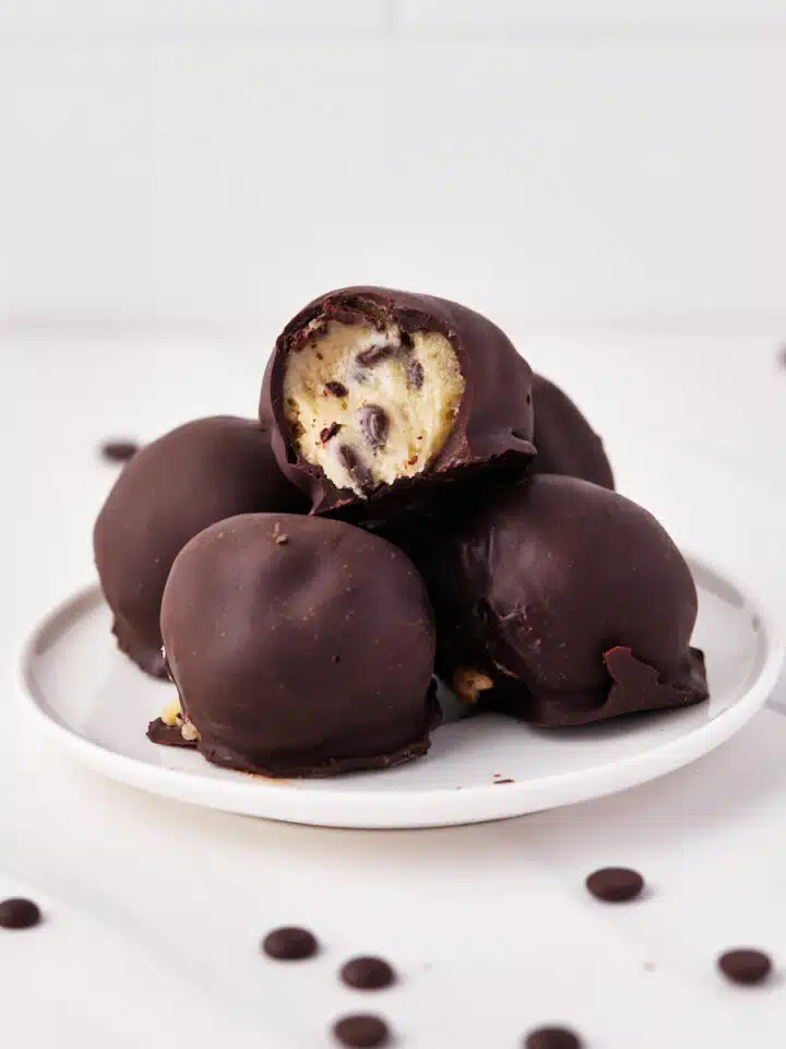 chocolate covered cookie dough bites on a small plate, surrounded by chocolate chips.