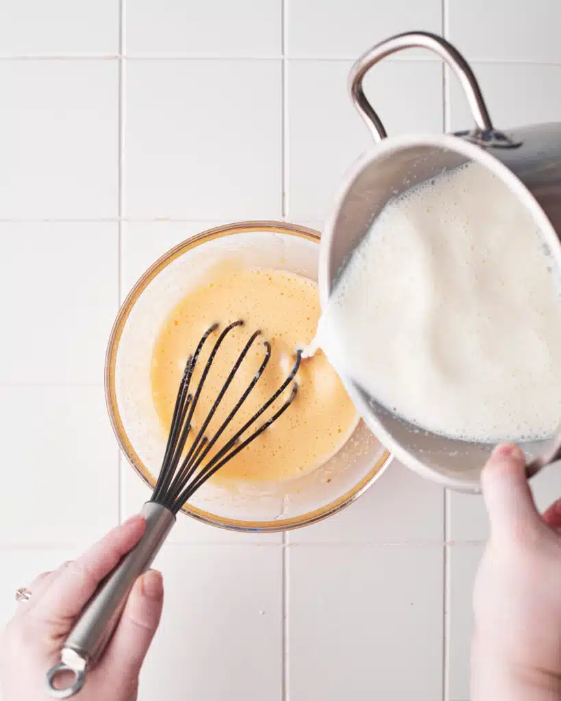 pouring hot milk into egg yoks to make custard.