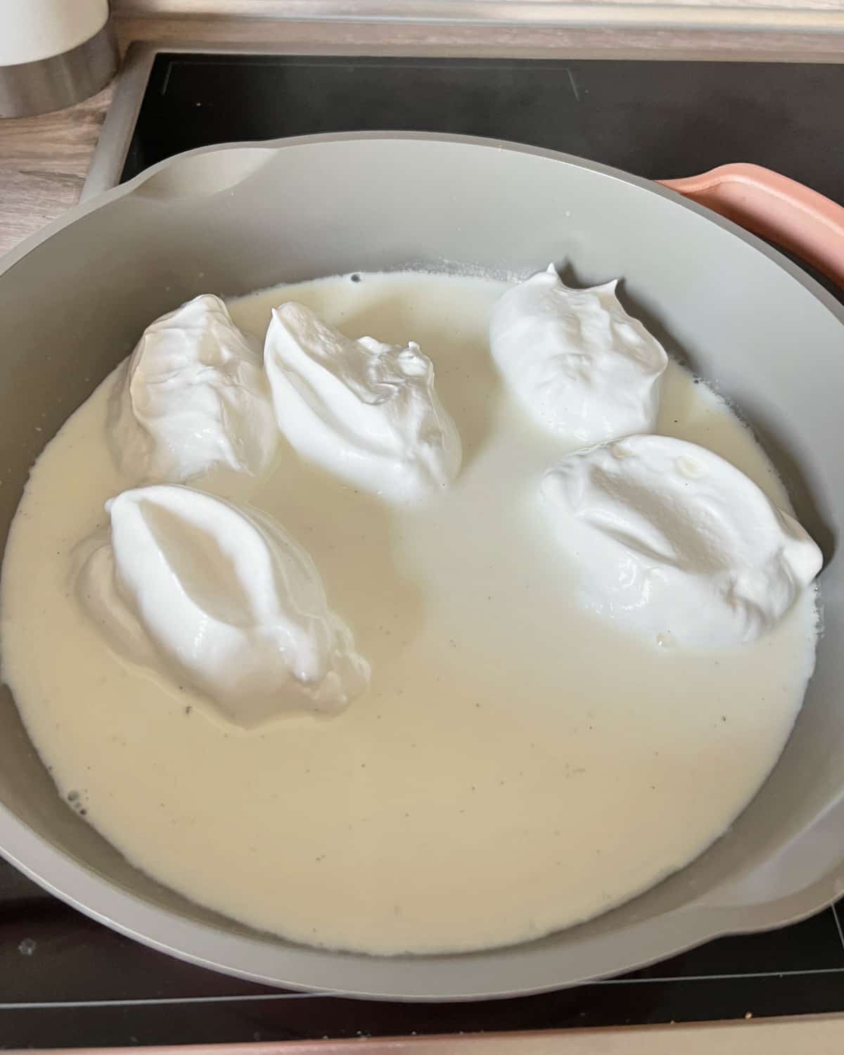 poaching meringues in hot milk to make floating island dessert.