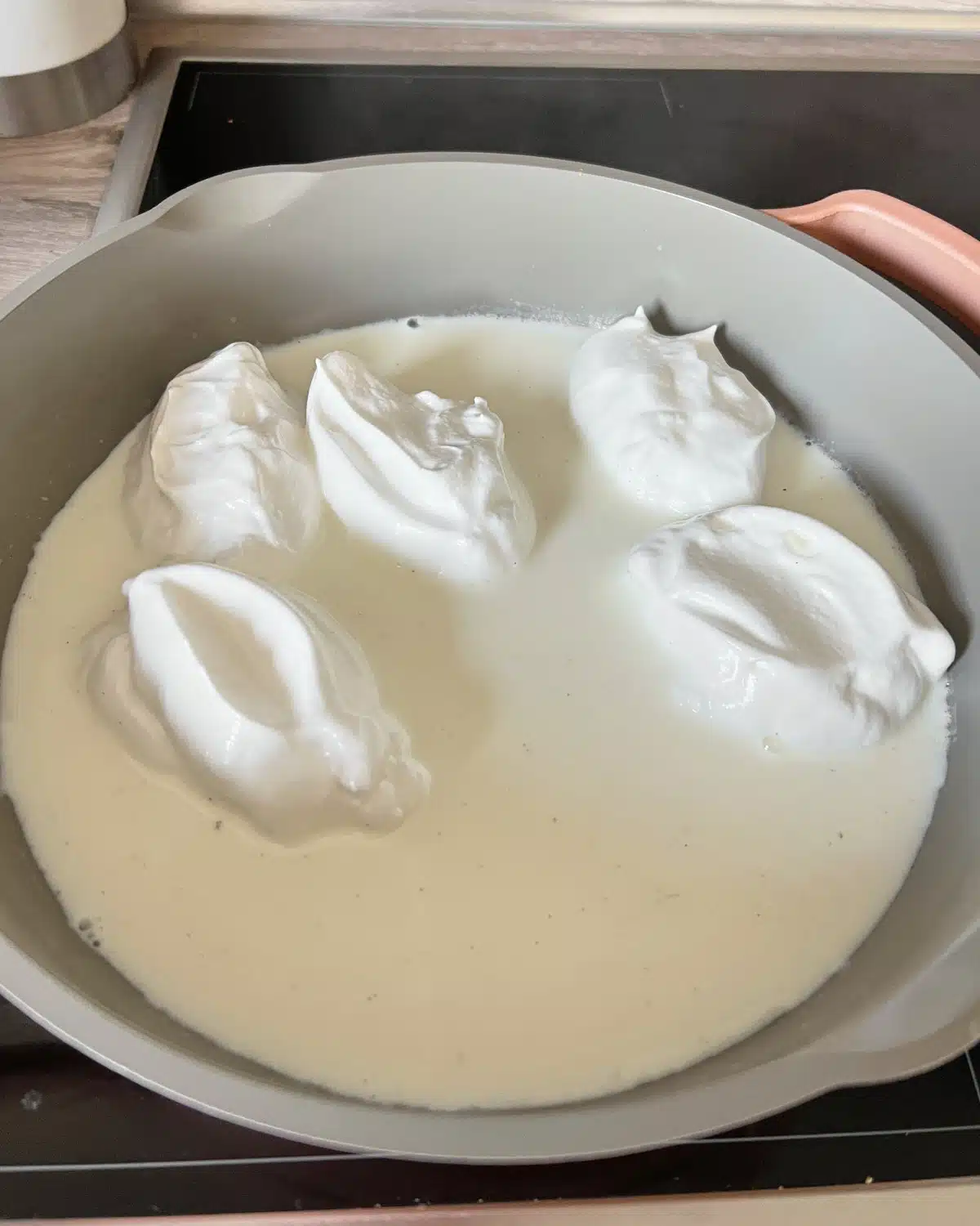 poaching meringues in hot milk to make floating island dessert.