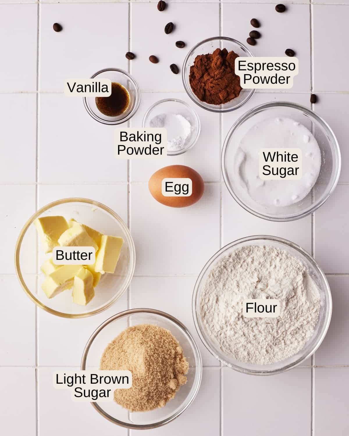 Labelled ingredients for coffee cookies, including espresso powder, vanilla, baking powder, egg, white sugar, butter, light brown sugar, and flour.
