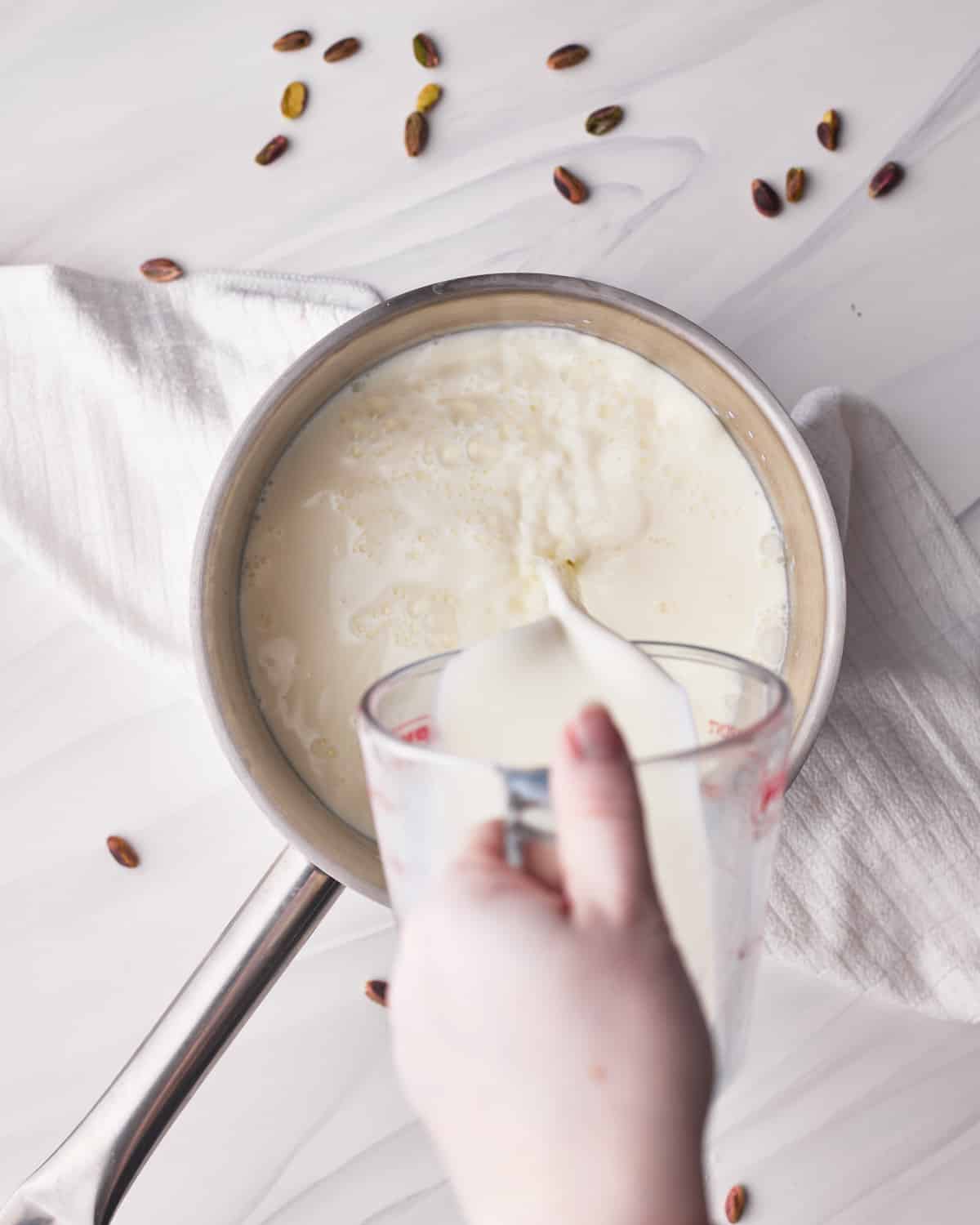Pouring milk into a saucepan to make pistachio custard.