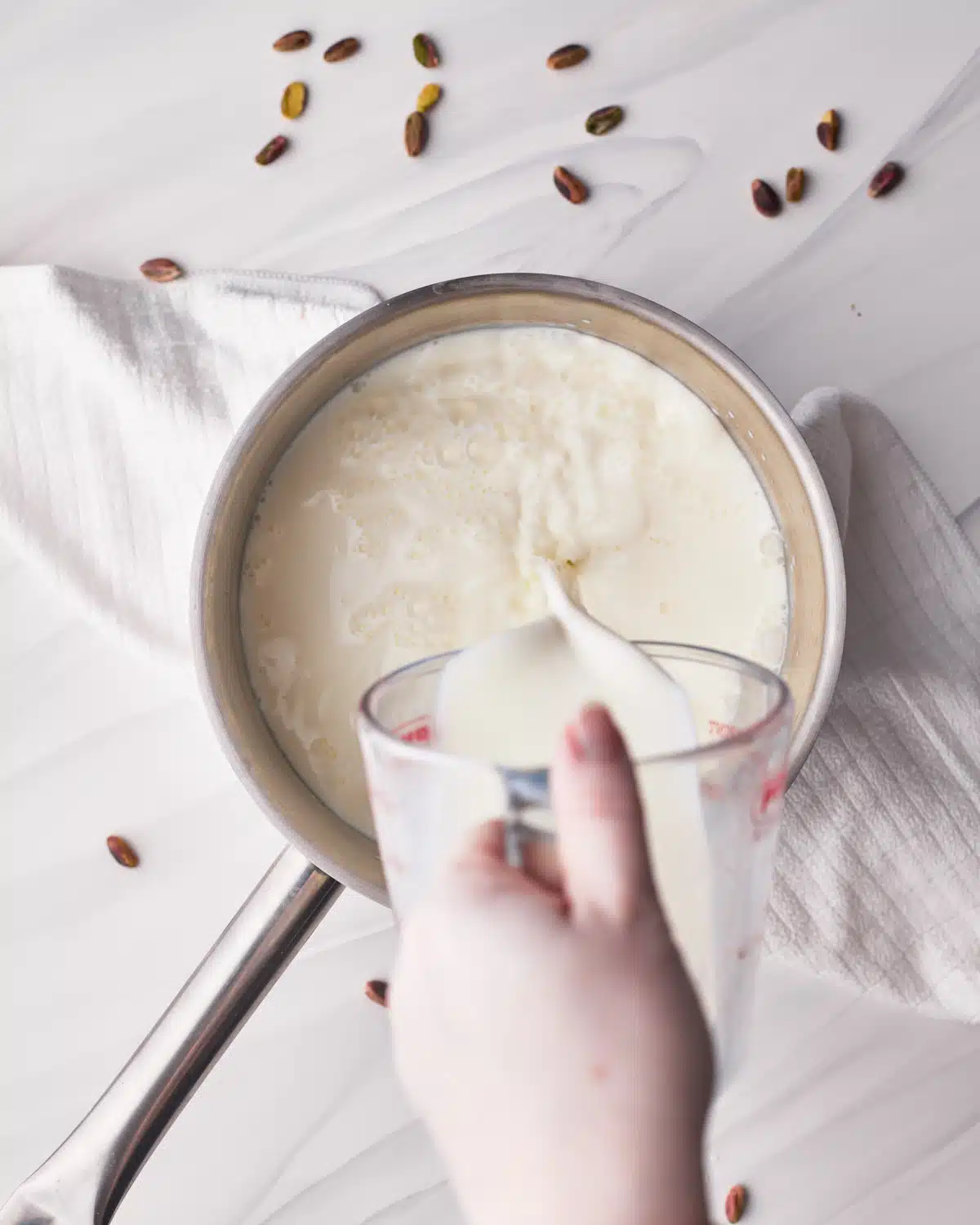 Pouring milk into a saucepan to make pistachio custard.
