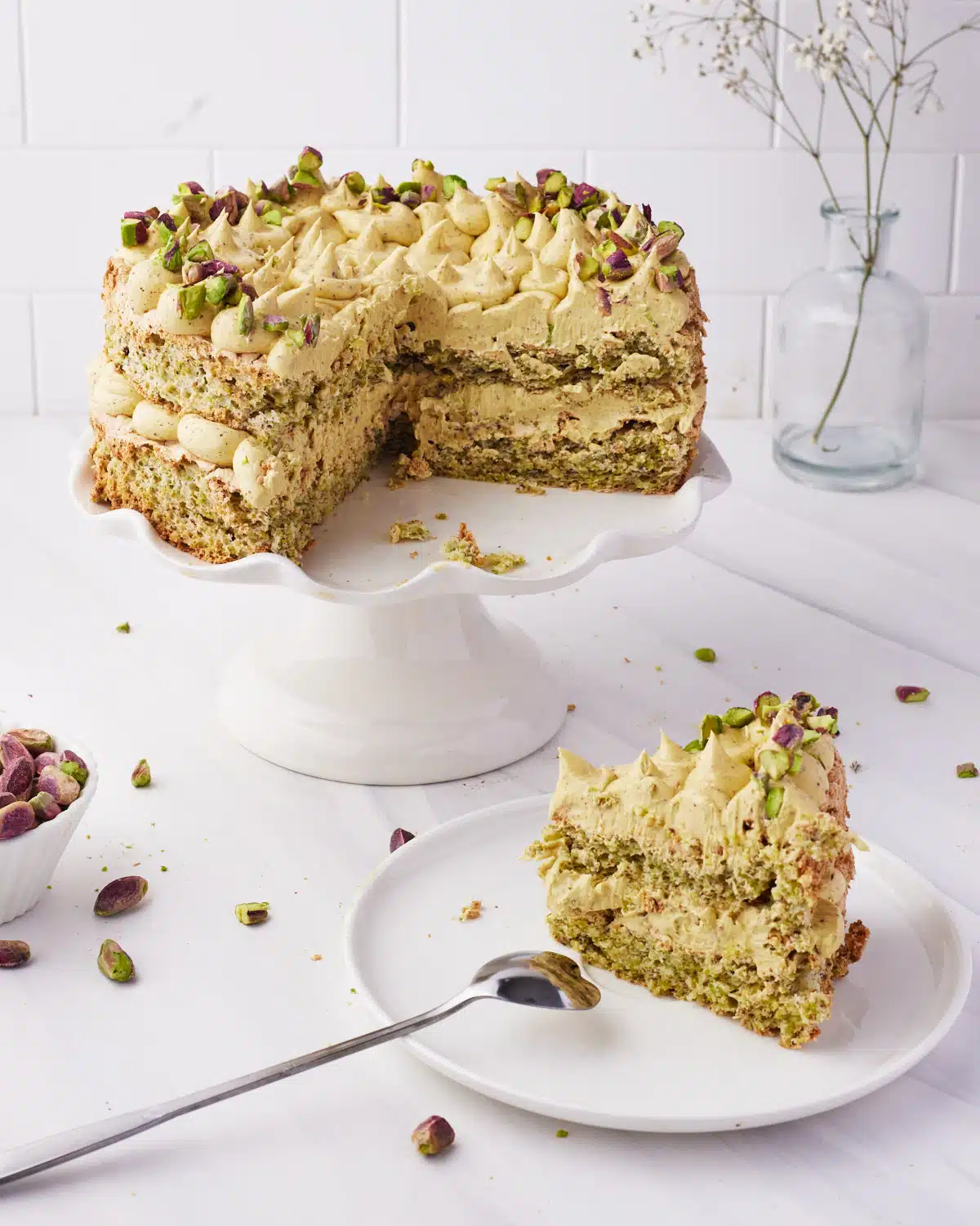 slice of pistachio dacquoise cake sitting on a plate next to the whole cake. 