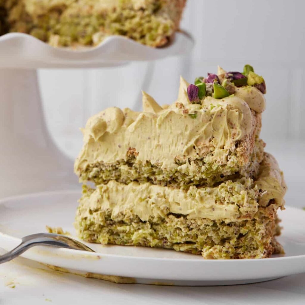 Slice of pistachio dacquoise cake on a plate showing the crunchy, crumbly texture and silky smooth pistachio buttercream.