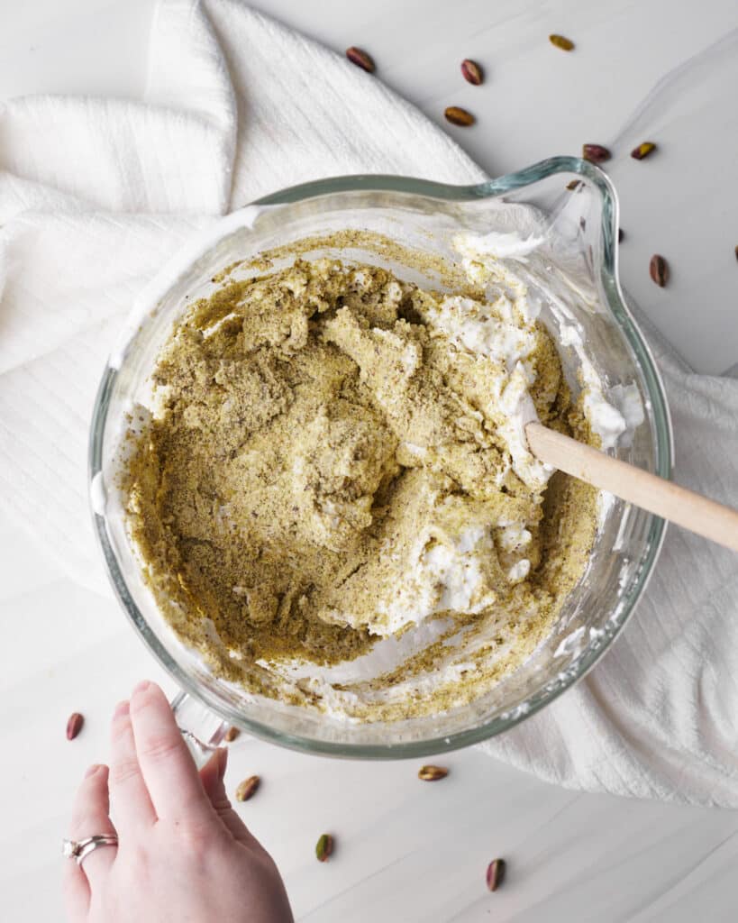 adding pistachio flour to. meringue to make pistachio dacquoise.