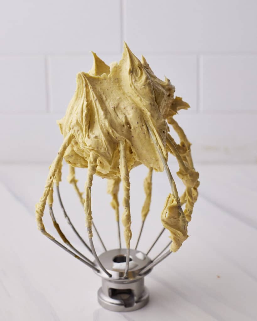Glossy pistachio French buttercream on a whisk.