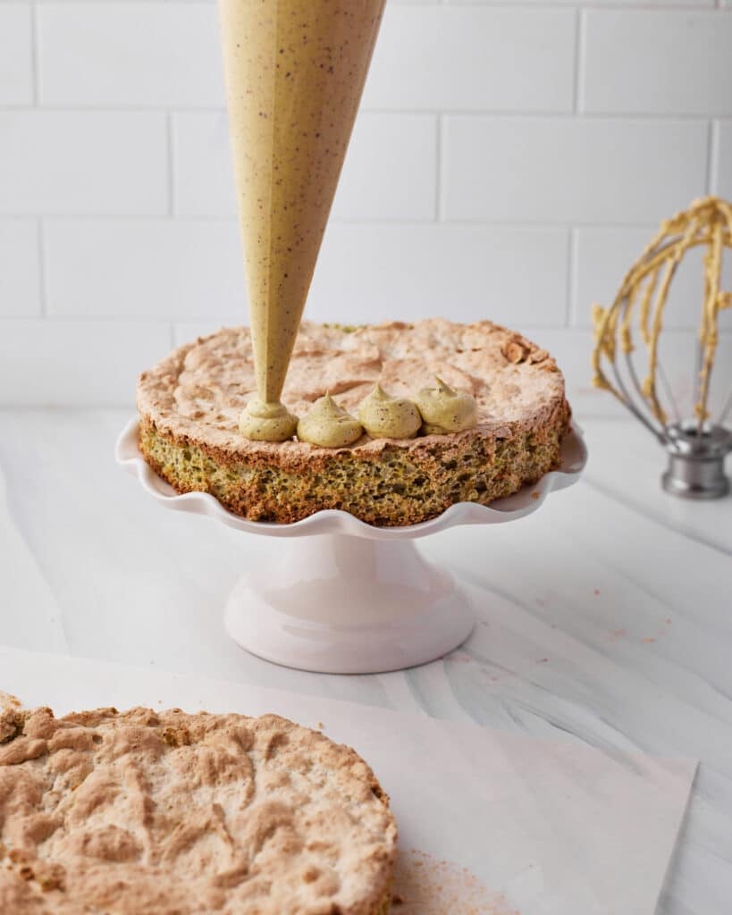 Piping french buttercream onto pistachio dacquoise cake.