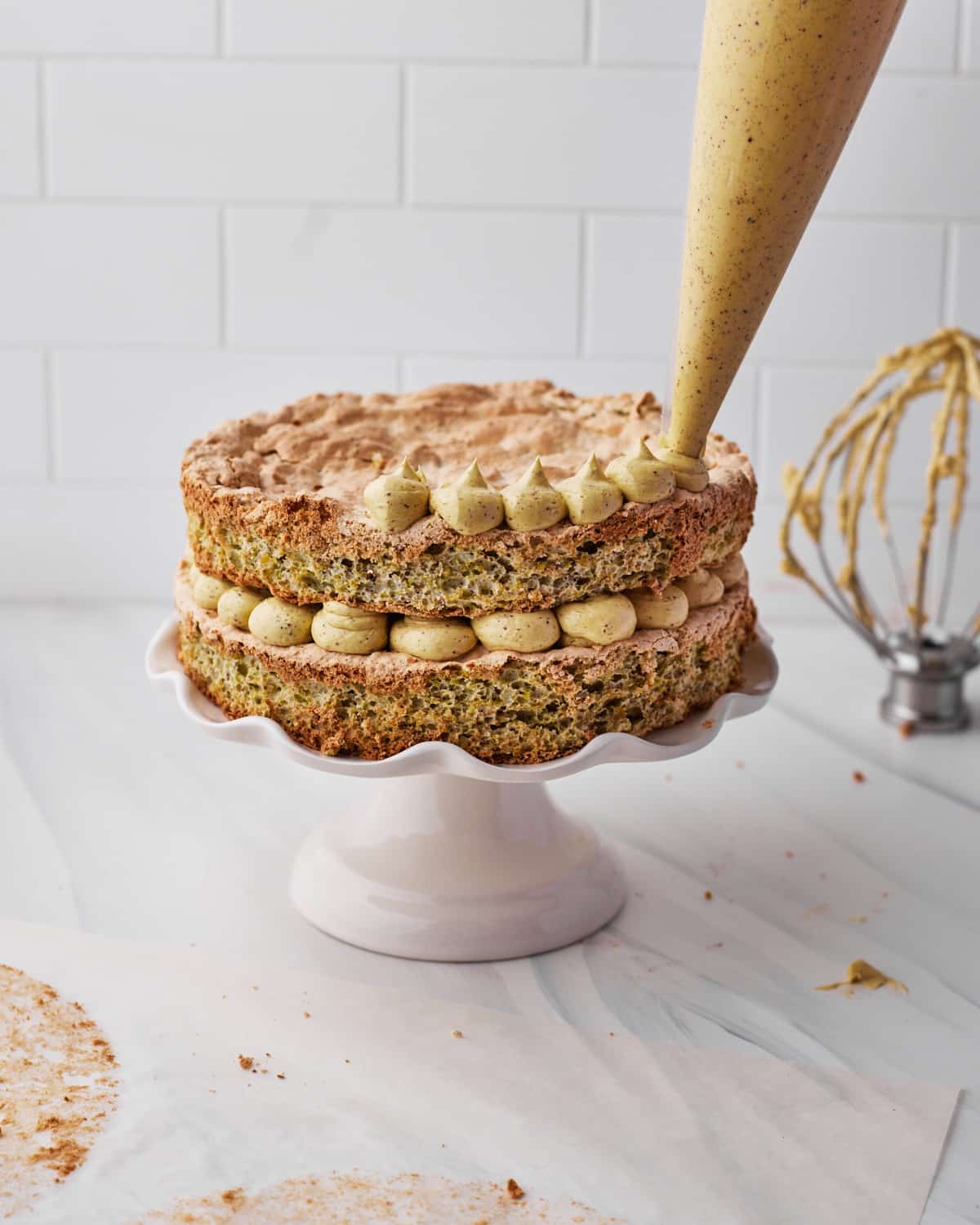 Piping french buttercream onto pistachio dacquoise cake.
