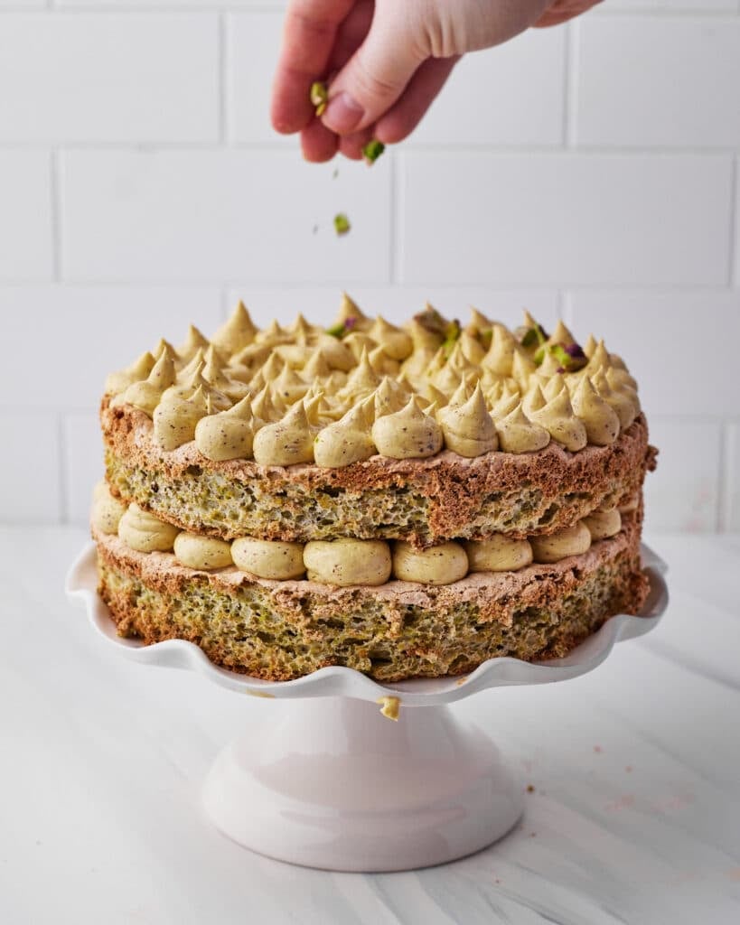 sprinkling chopped pistachios on top of pistachio dacquoise cake to decorate.