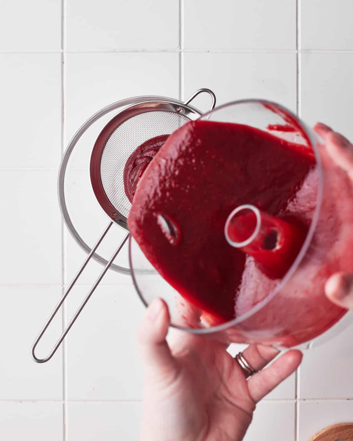 pouring strawberry puree through a sieve to remove the seeds. 