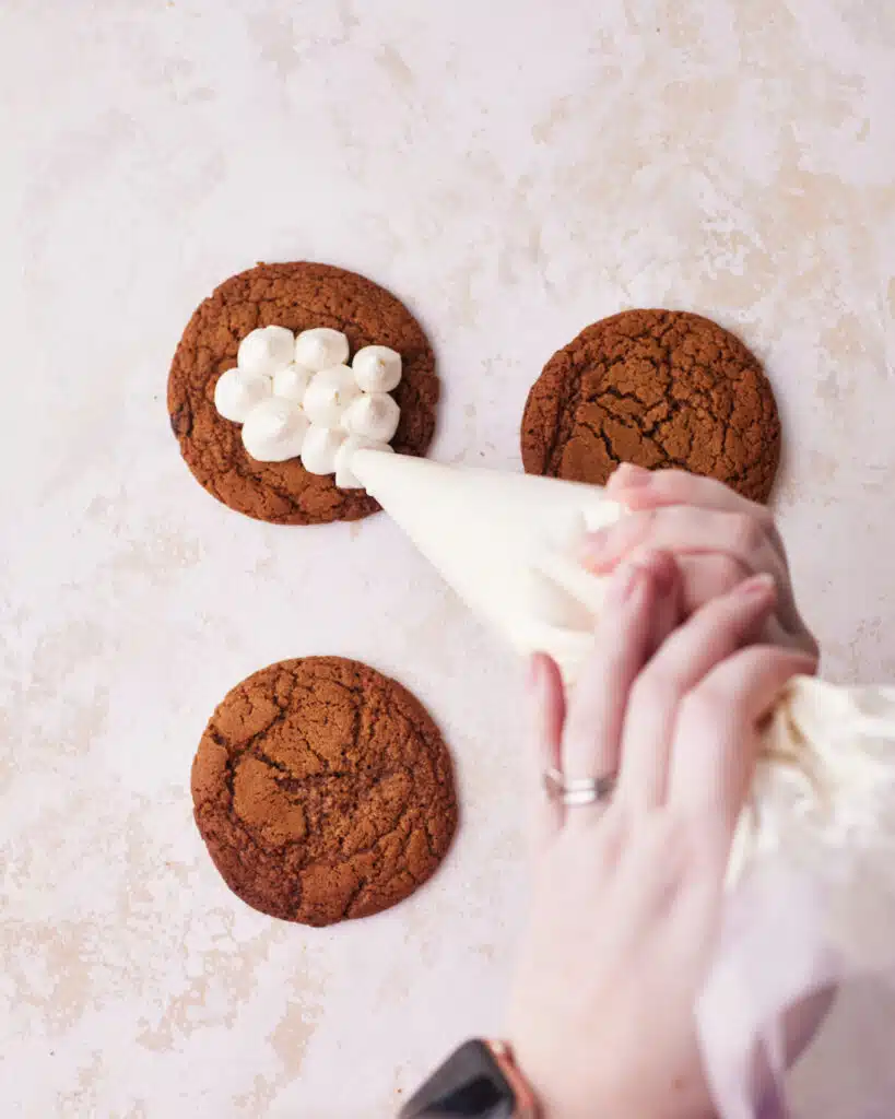 Piping mascarpone cream onto espresso cookies to make tiramisu cookies.
