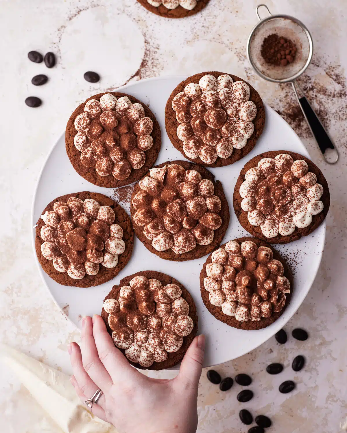Tiramisu cookies on a plate with a hand about to pick one up. 