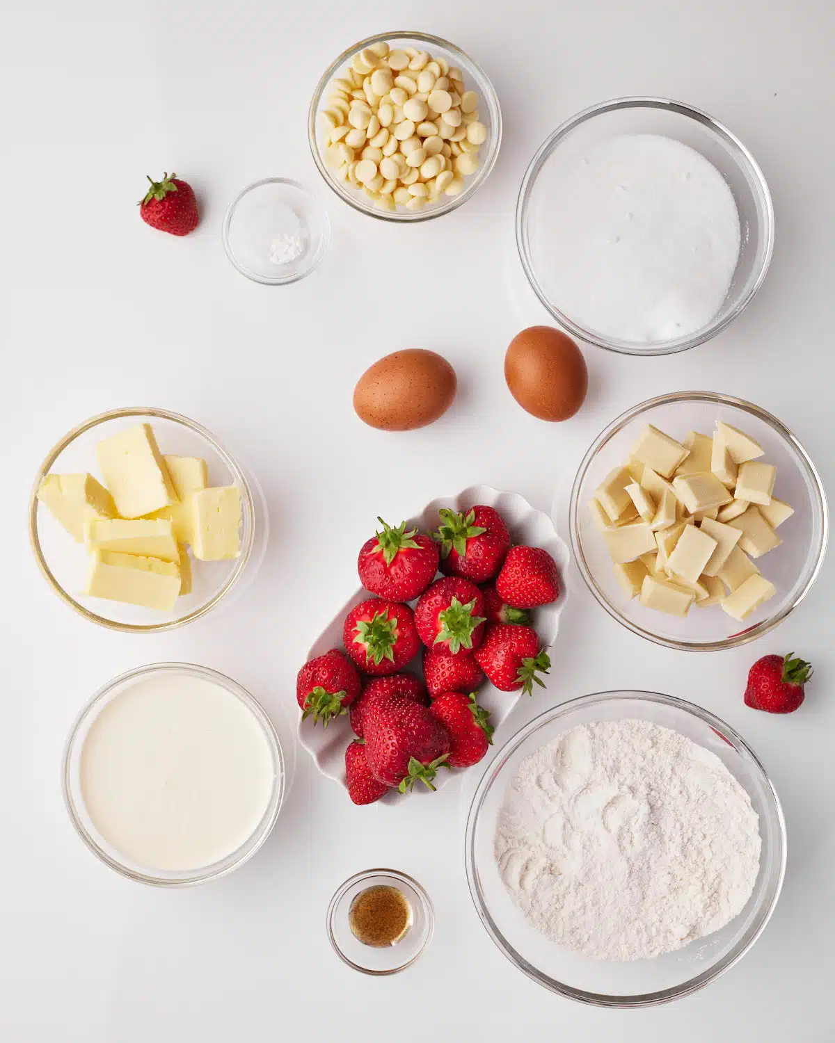 Ingredients to make strawberry brownies, strawberries, sugar, white chocolate, eggs, flour, butter and heavy cream. 