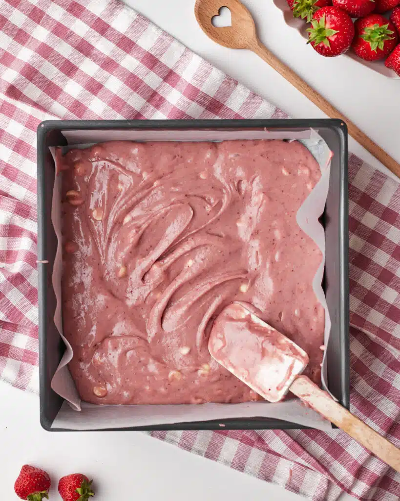 process shot for strawberry brownies, pink brownie batter being poured into the square cake tin, ready to be baked.