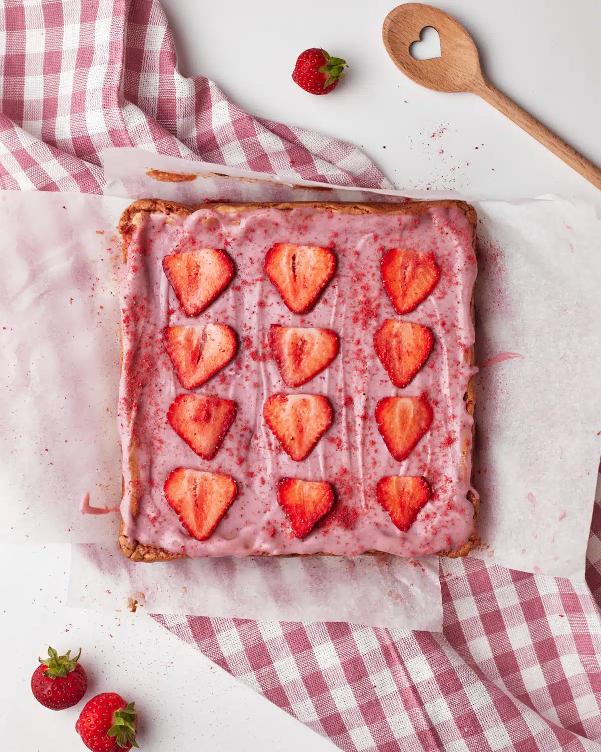 process shot of decorating strawberry brownies with strawberry ganache, topped with fresh strawberry slices and freeze-dried strawberries.