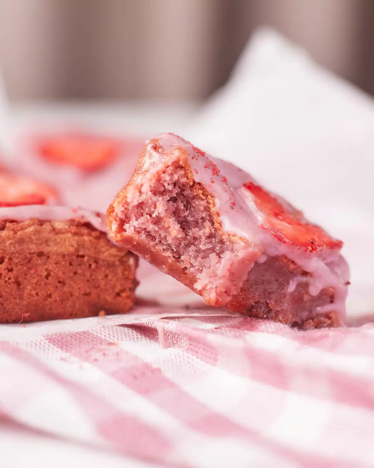 close up of a strawberry brownie with a bite taken out to reveal the pink inside. 