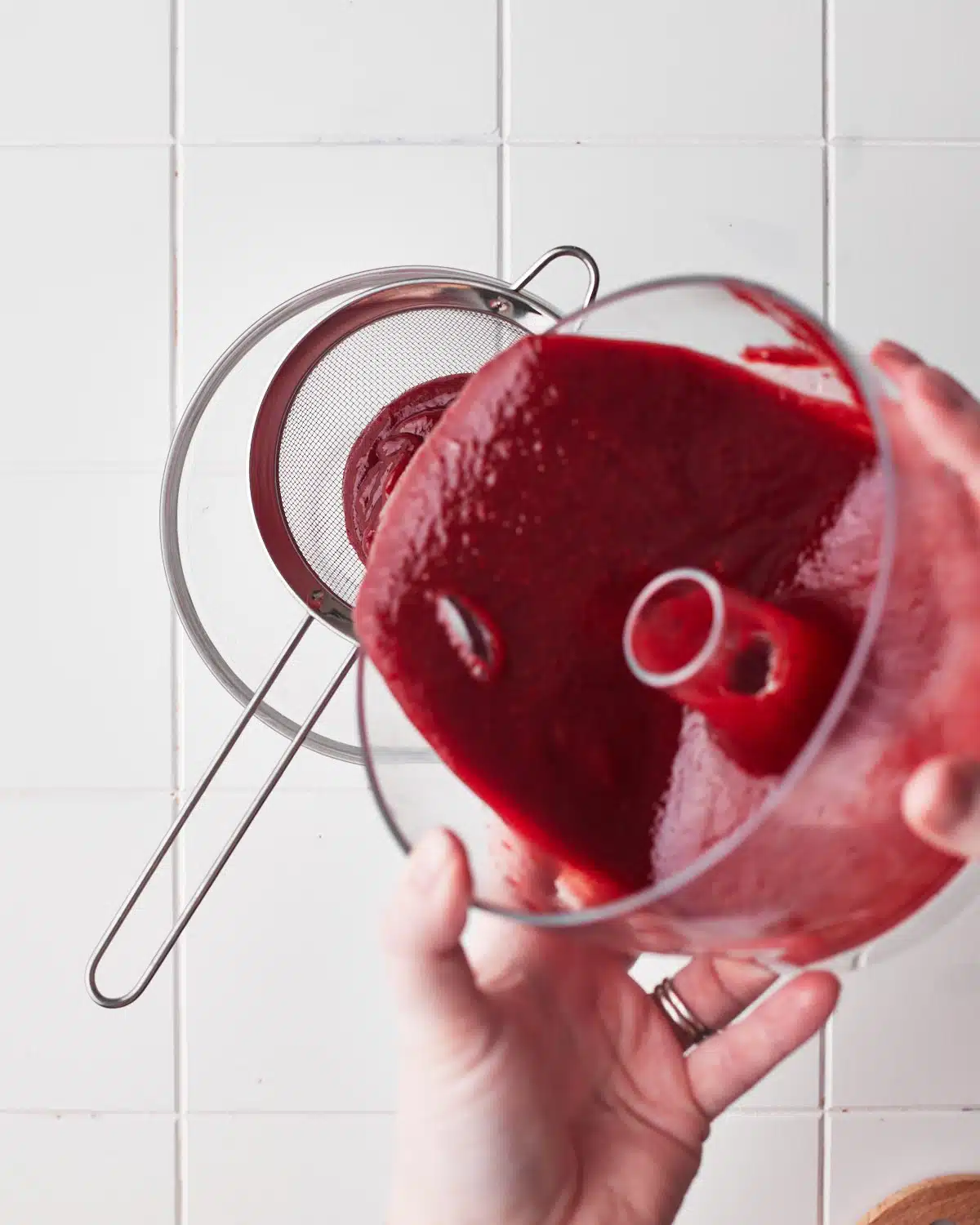 passing strawberry puree through a fine mesh sieve to make strawberry coulis.