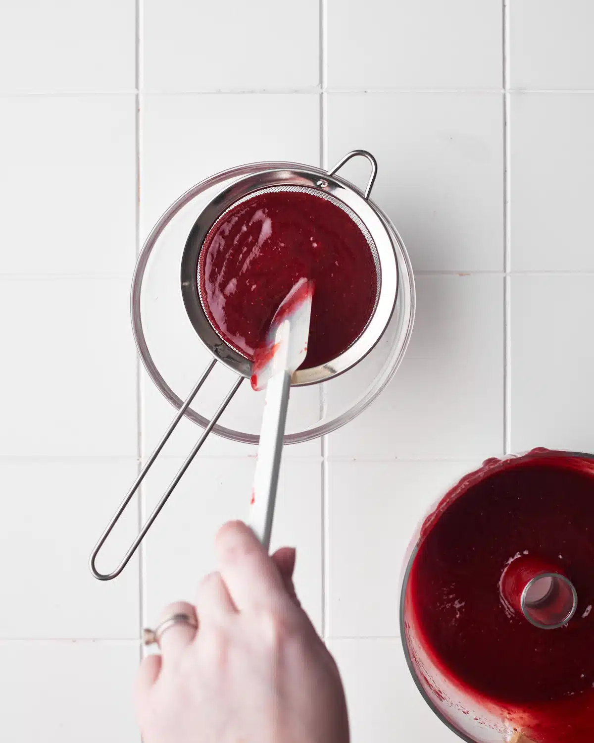 passing strawberry puree through a fine mesh sieve to make strawberry coulis.