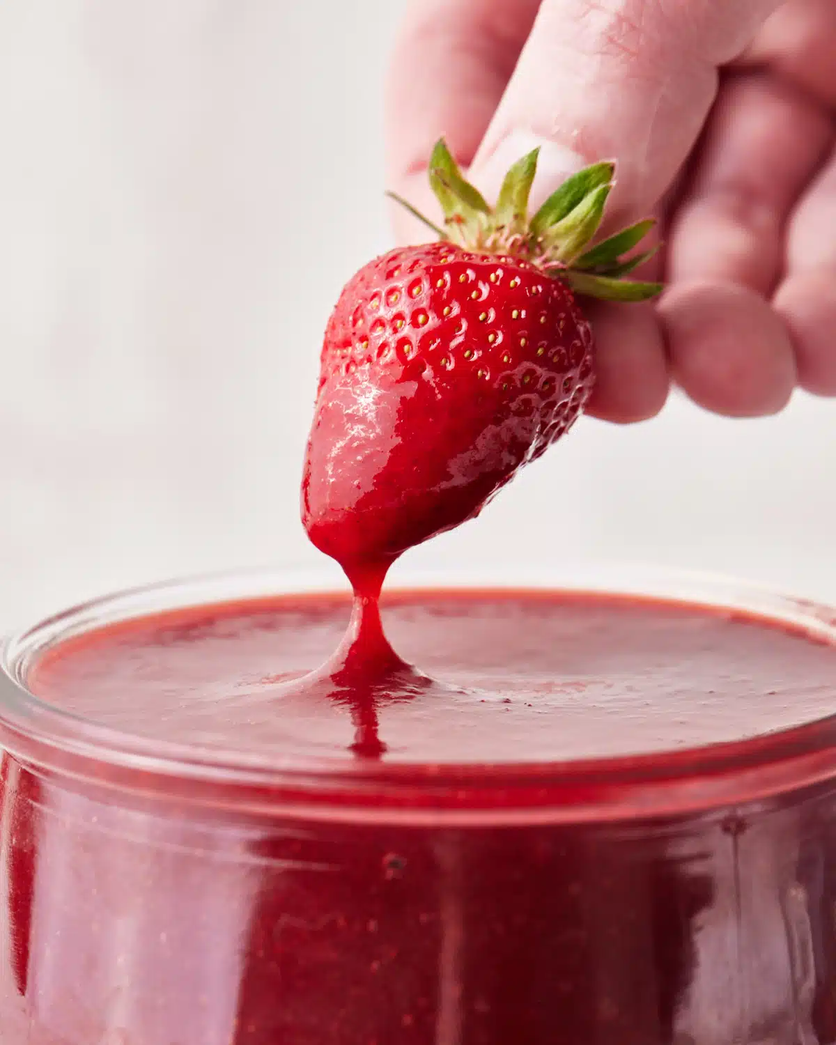 close up of a fresh strawberry being dipped into strawberry puree. 