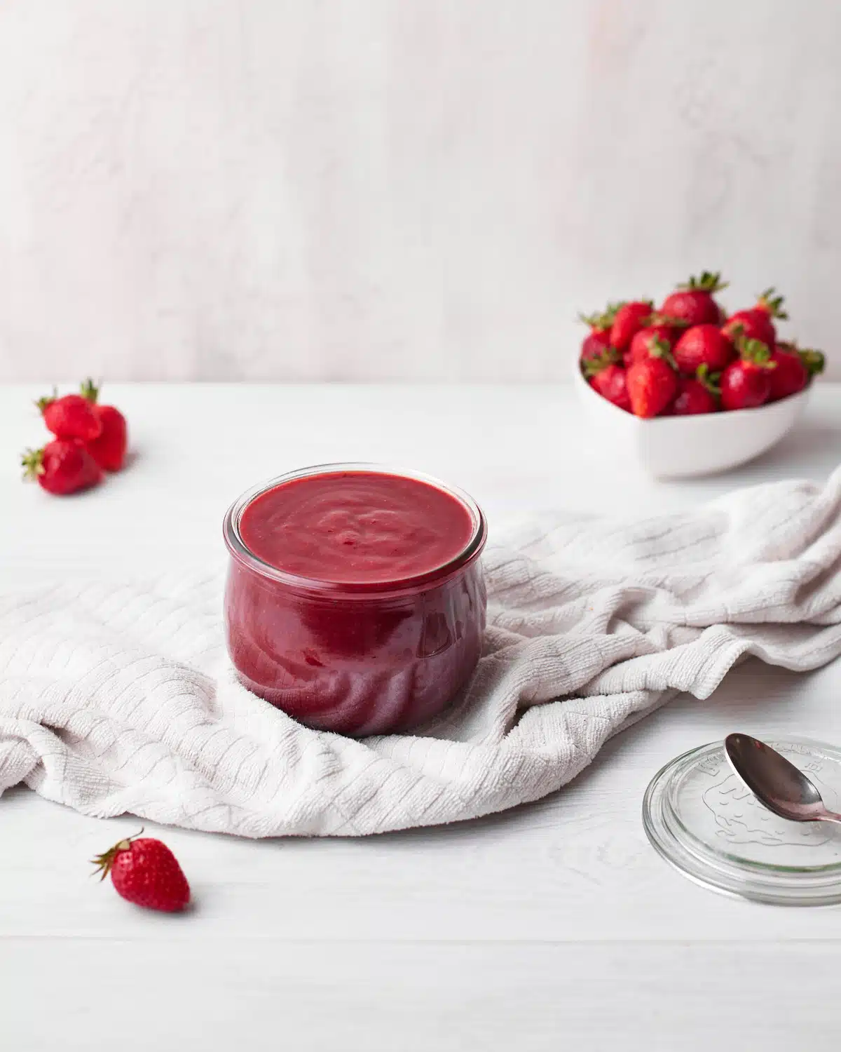 strawberry puree (strawberry coulis) in a glass jar with fresh strawberries all around. 