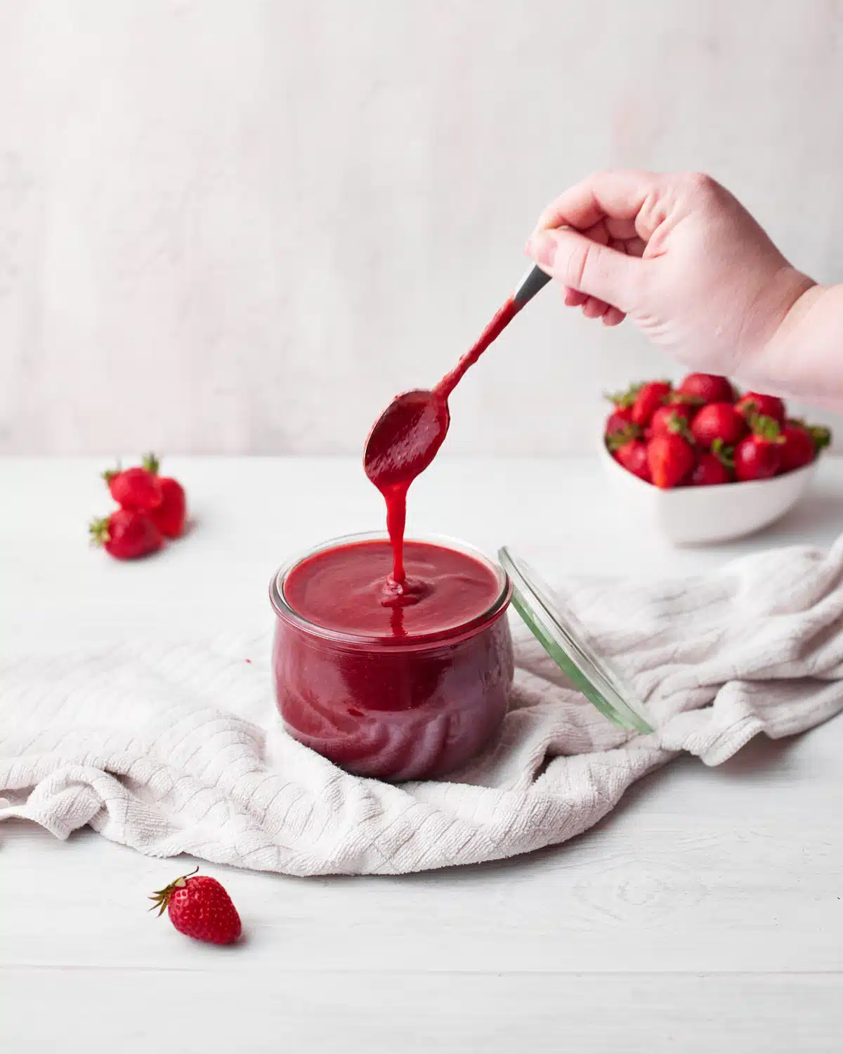 strawberry puree in a glass jar, with a spoon drizzling some of it back into the jar.