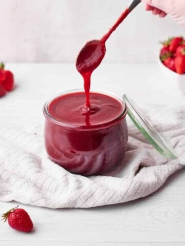 strawberry puree in a glass jar, with a spoon drizzling some of it back into the jar.