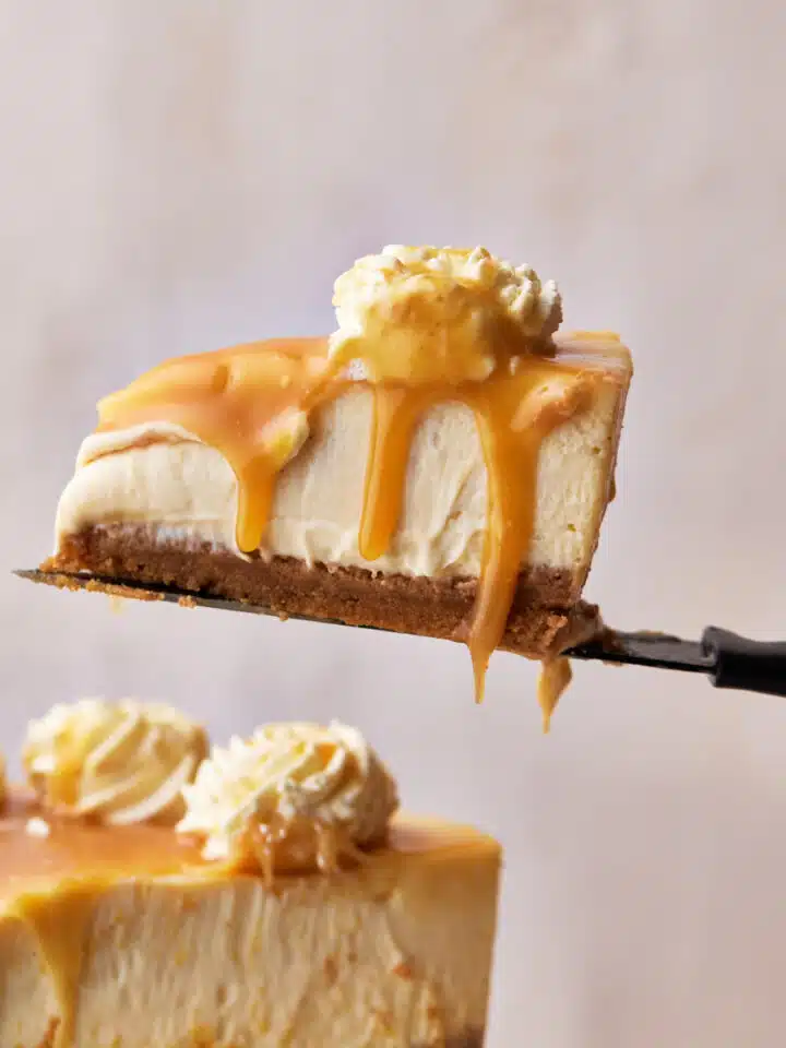 slice of caramel cheesecake being lifted up on a knife, with caramel sauce dripping off the edge.