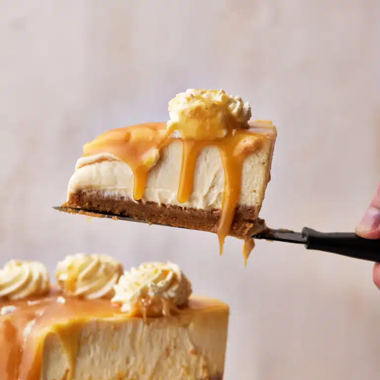 slice of caramel cheesecake being lifted up on a knife, with caramel sauce dripping off the edge.