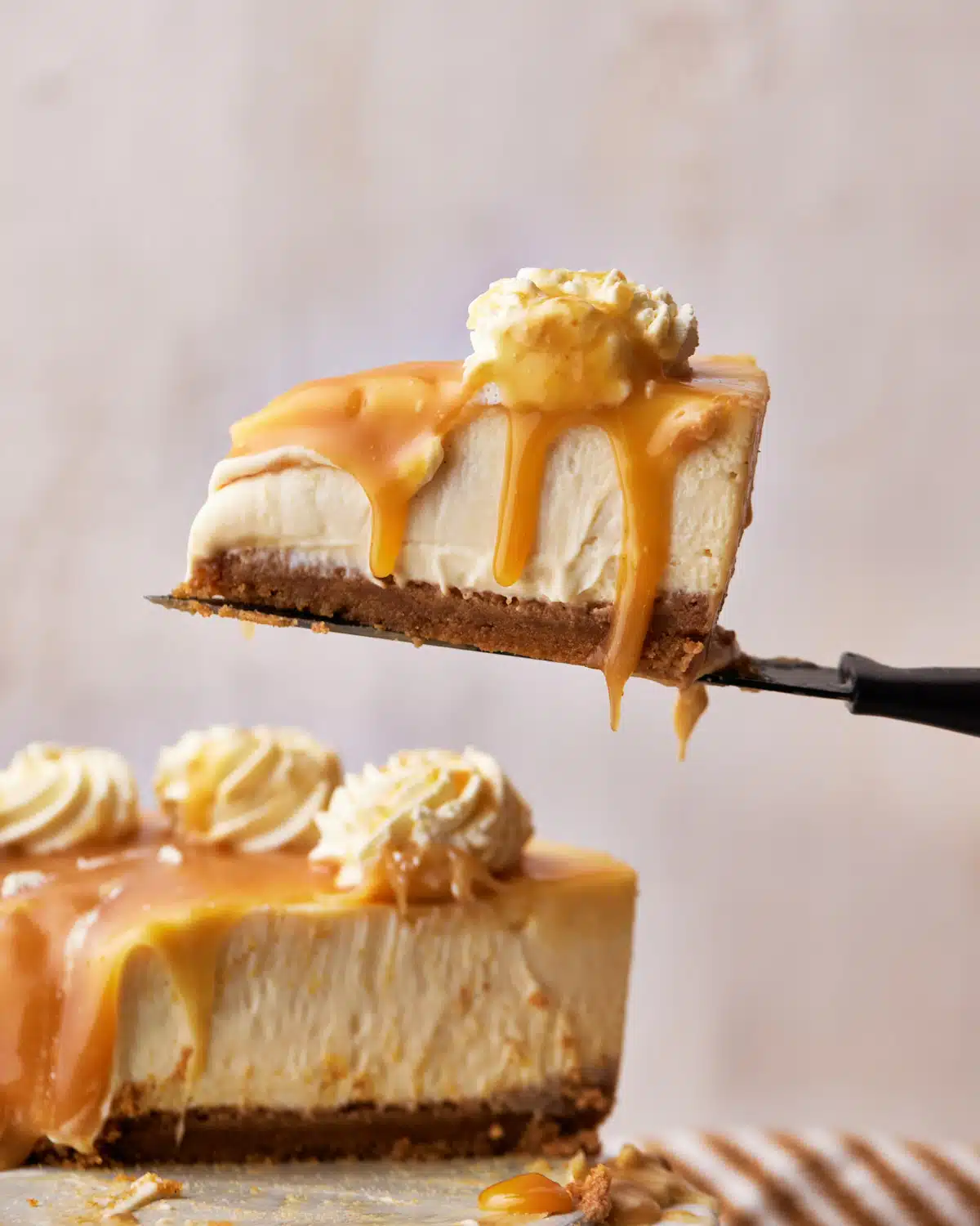 slice of caramel cheesecake being lifted up on a knife, with caramel sauce dripping off the edge.