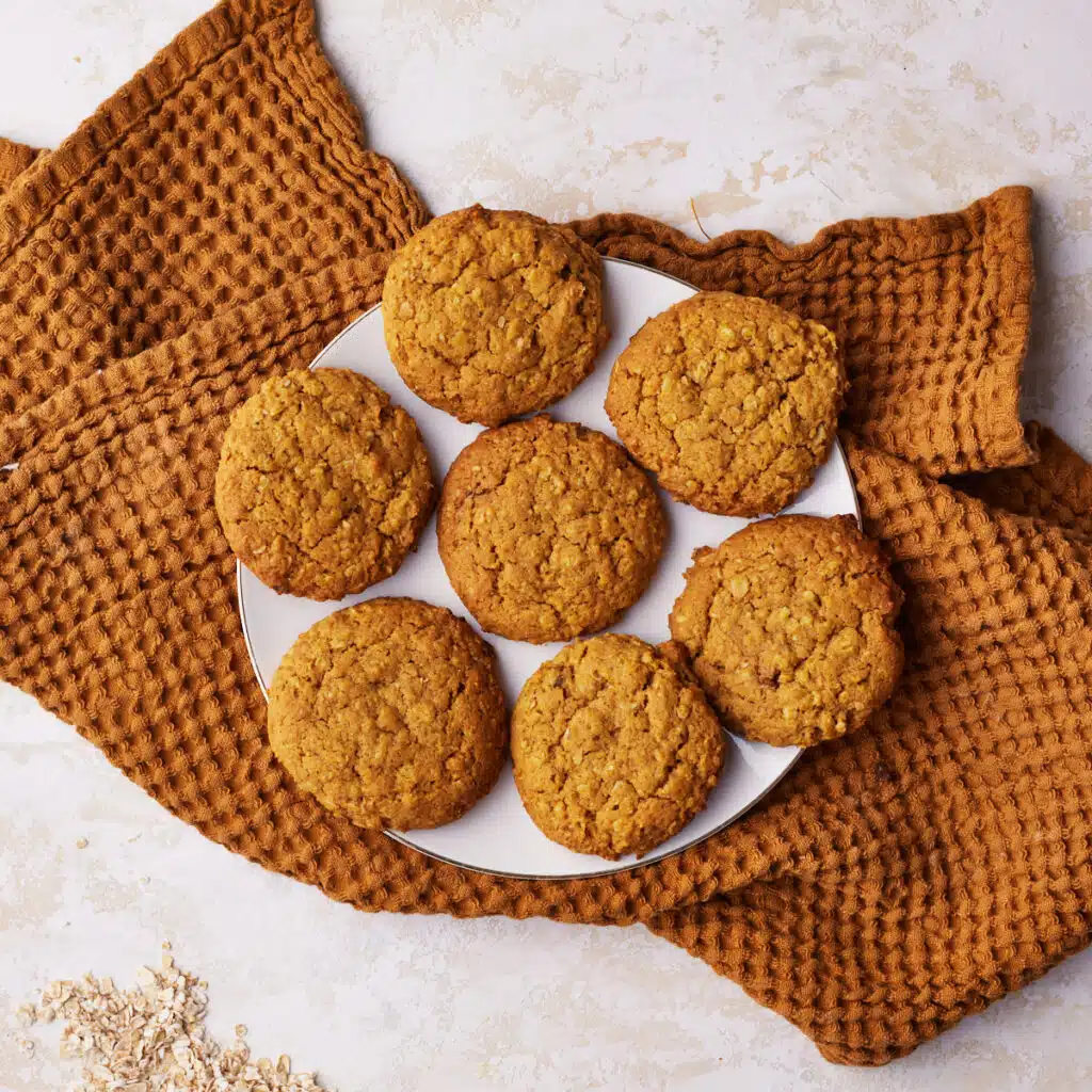 Seven pumpkin oatmeal cookies on a plate, with a cloth underneath the plate.