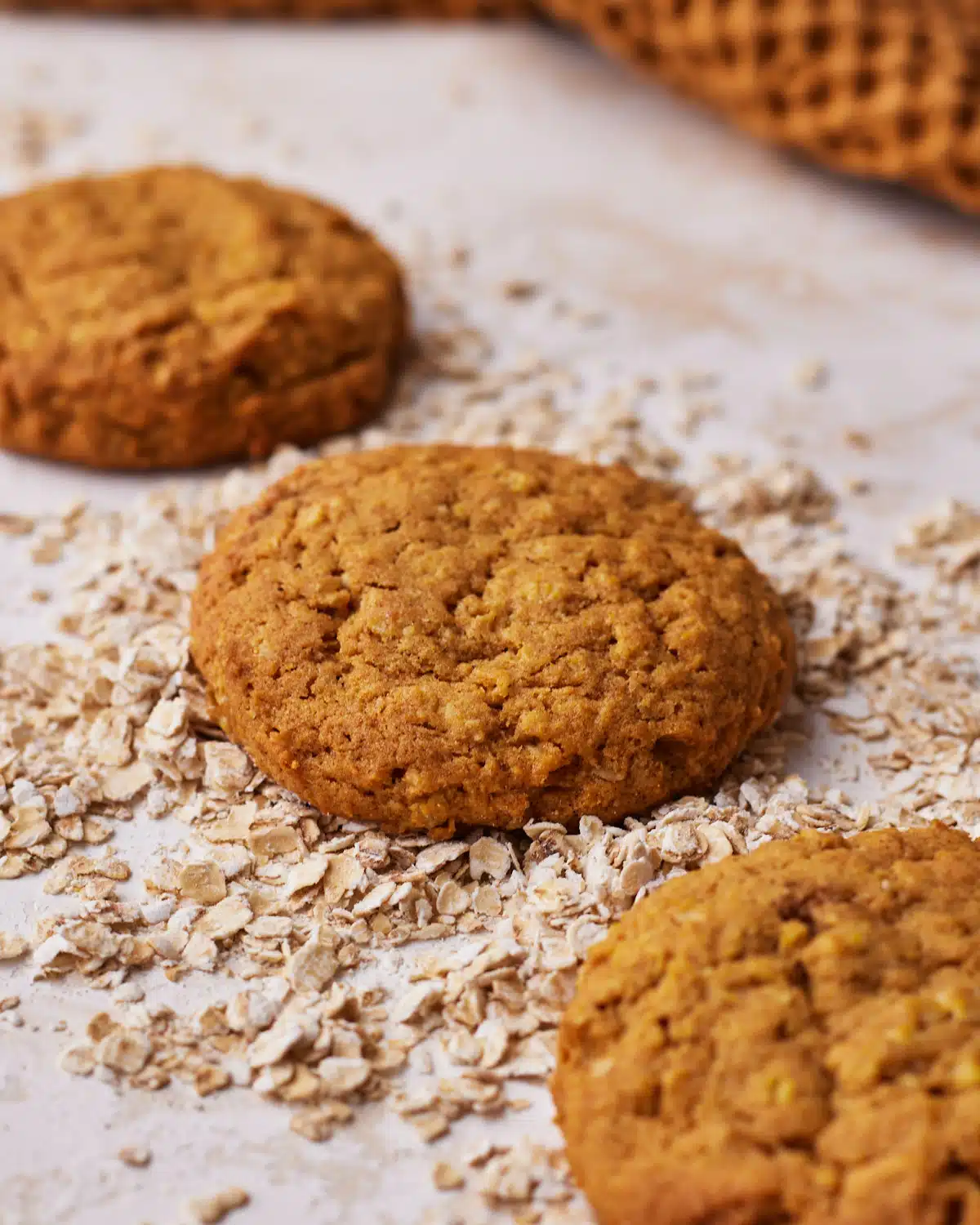 Three pumpkin oatmeal cookies in a line, on top of some oats. 