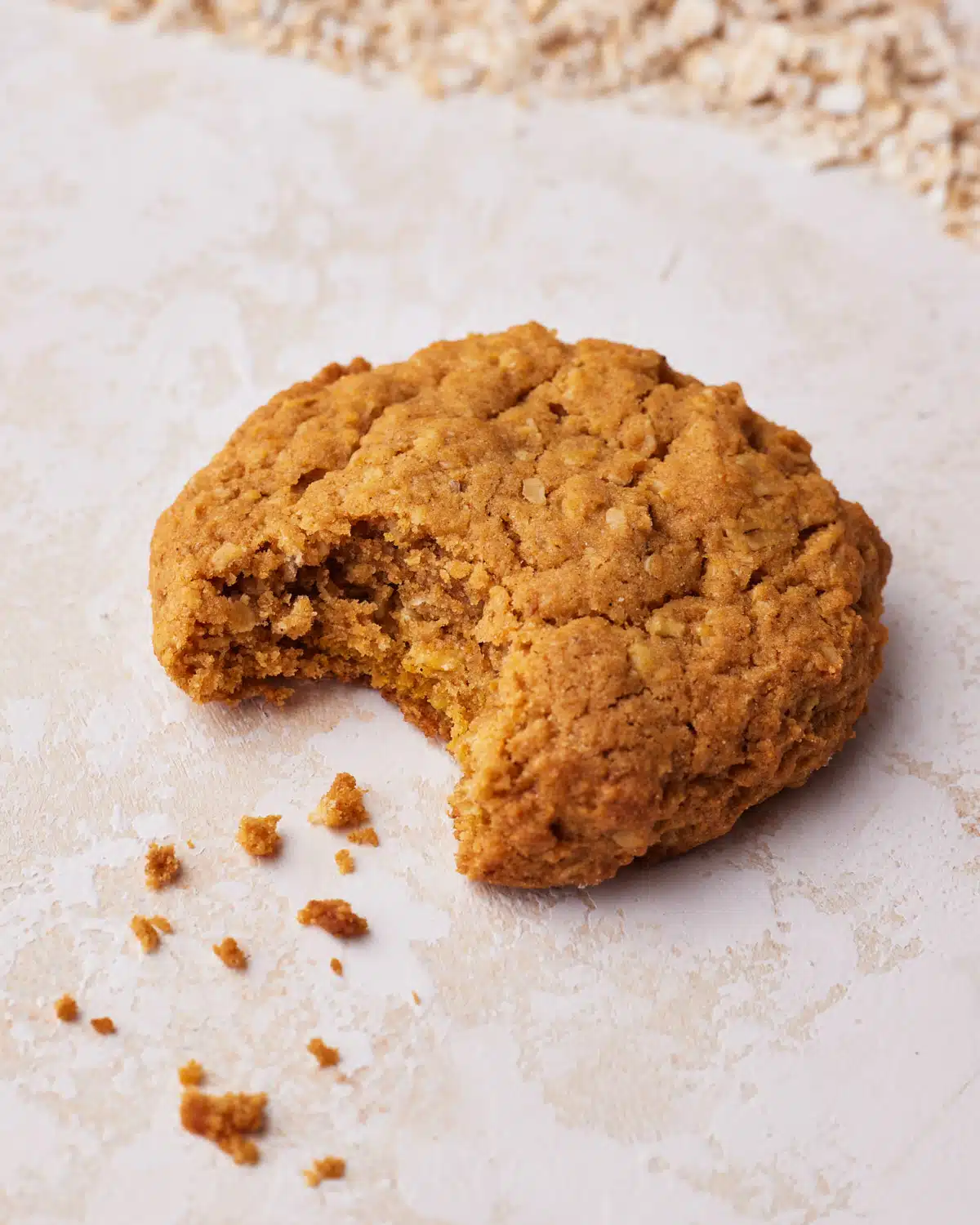 Single pumpkin oatmeal cookie with a bite taken out, leaving a few crumbs behind. 