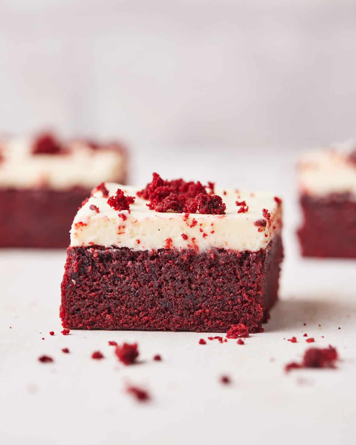 three red velvet brownies on a table with red velvet crumbs all around.