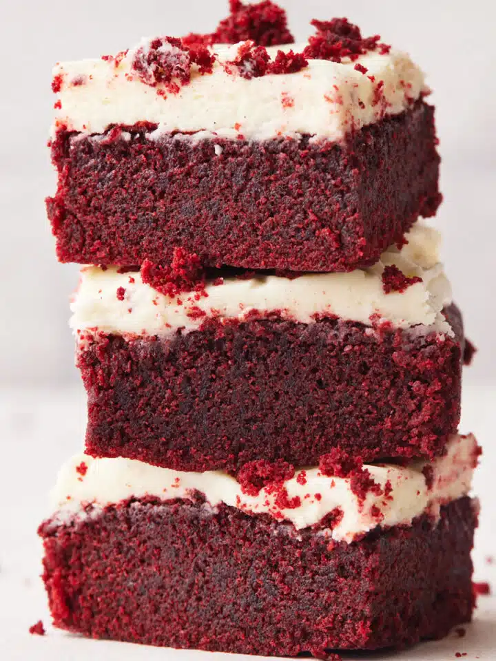 three red velvet brownies stacked on top of each other with cream cheese frosting.