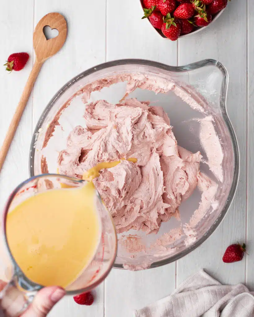 process shot of making strawberry cupcakes, adding eggs and milk to pretty pink cupcake batter.