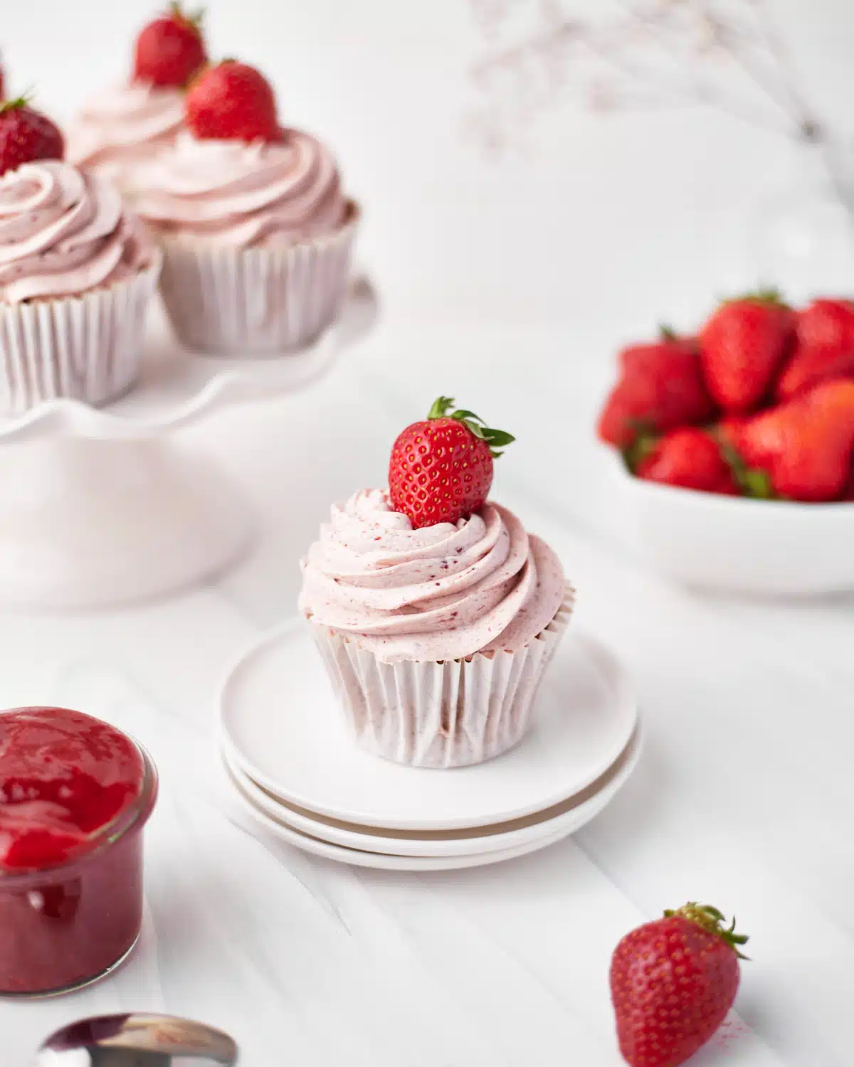 strawberry cupcake on a plate with strawberry buttercream and a whole strawberry on top. 