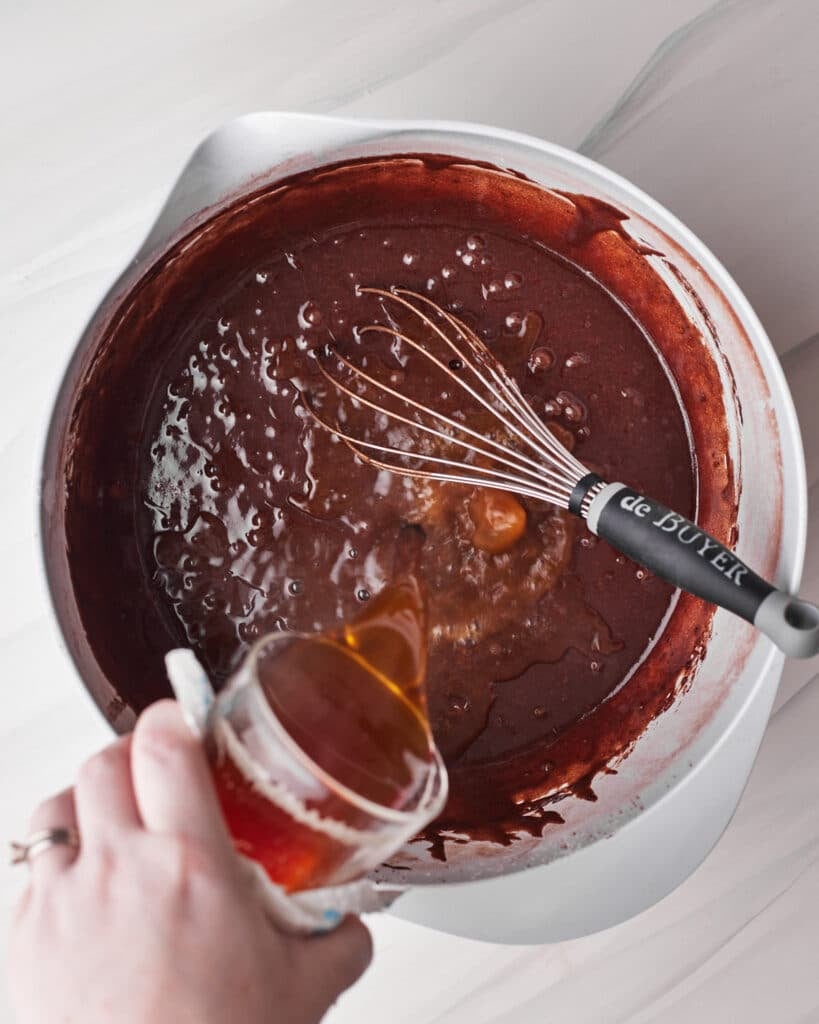 pouring hot water and espresso powder into cake batter to make tuxedo cake.