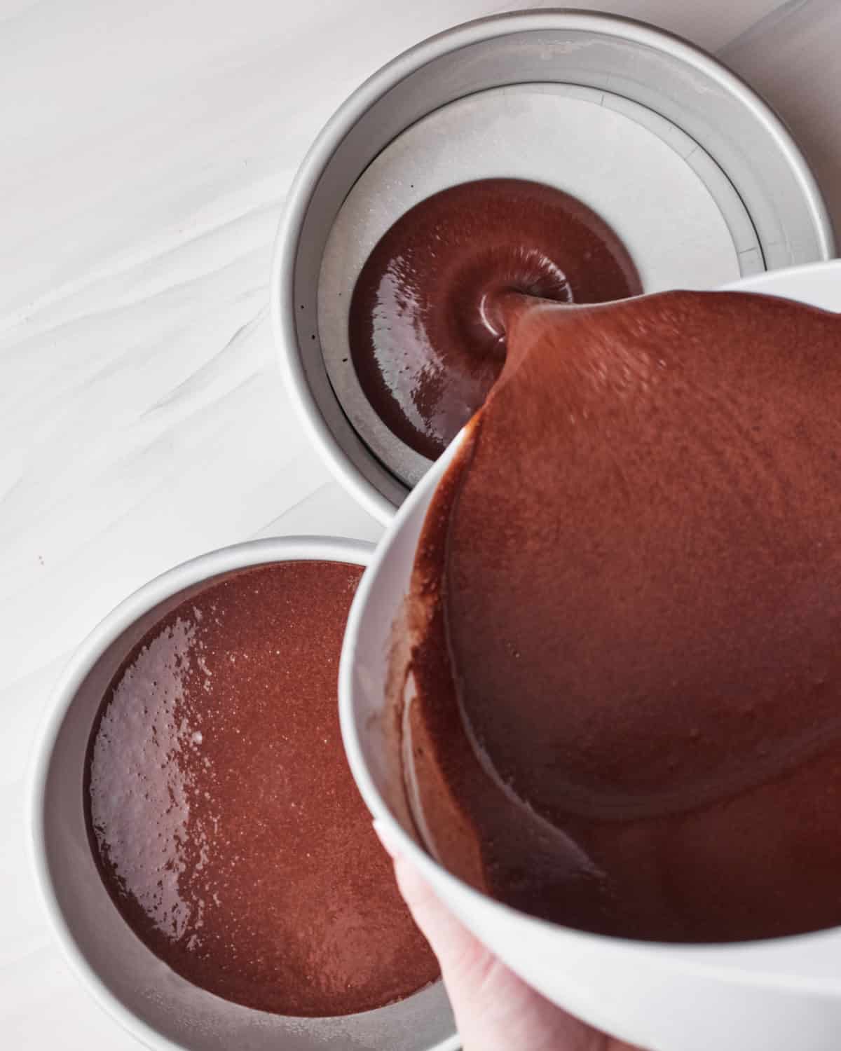 pouring chocolate cake batter into cake pans to make tuxedo cake.