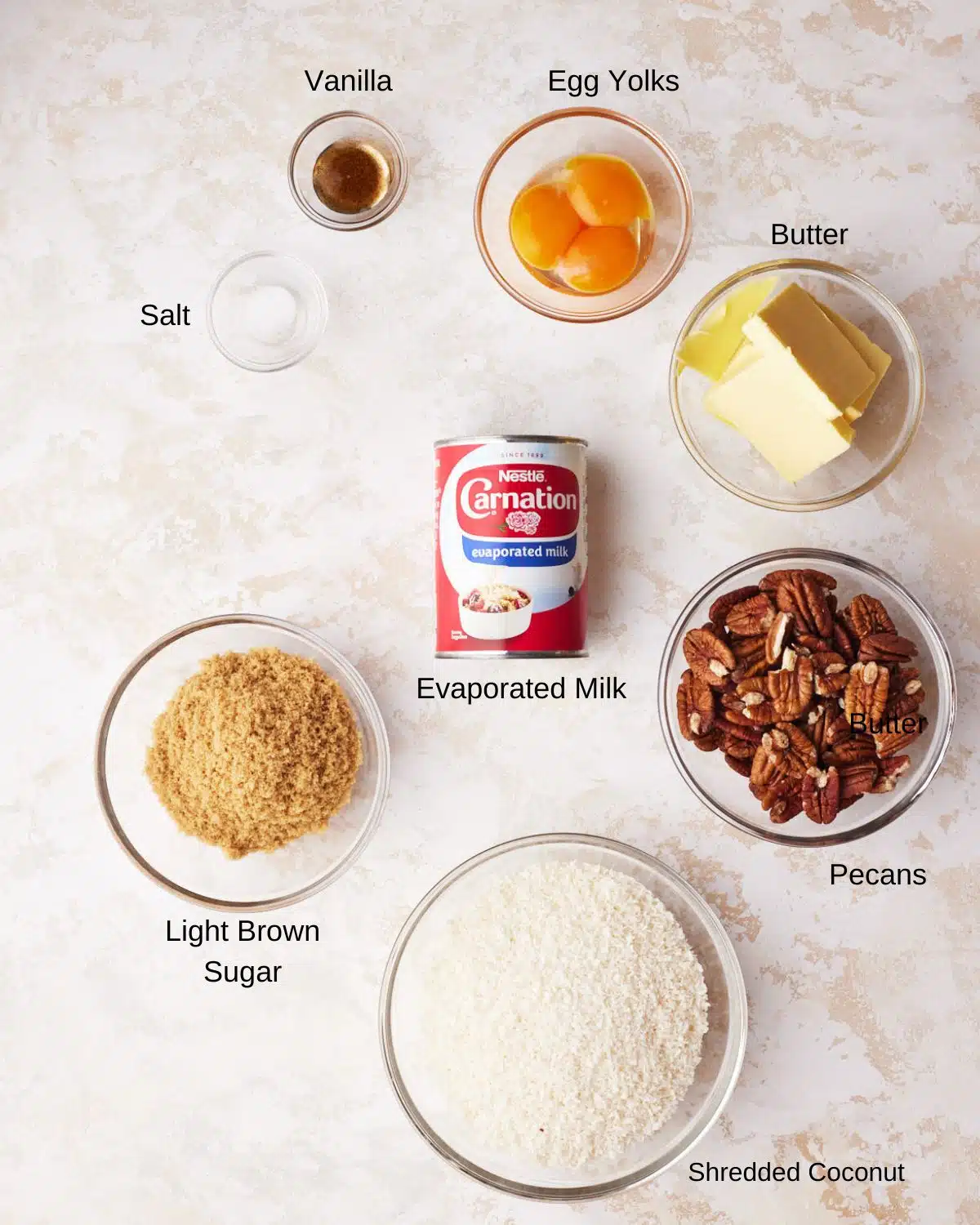 labelled ingredients shot of ingredients to make german chocolate frosting - coconut pecans, evaporated milk, butter, light brown sugar, egg yolks, salt and vanilla.