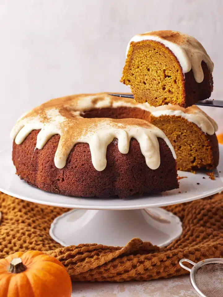 pumpkin bundt cake with cream cheese glaze with a slice being cut out of it.