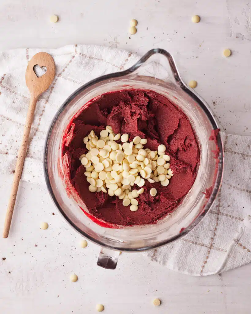 white chocolate chips being added to red velvet cookie dough.