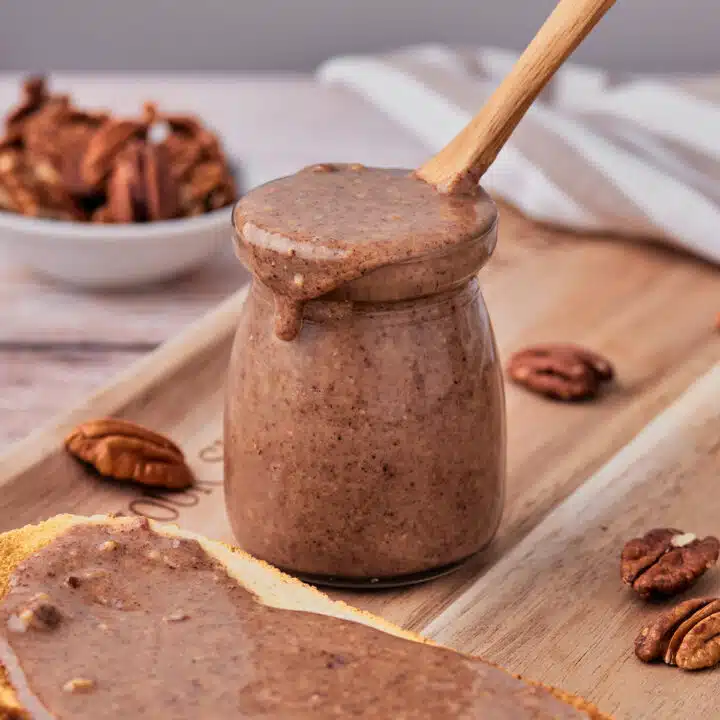 Pecan butter in a glass jar with a small wooden spoon in it.