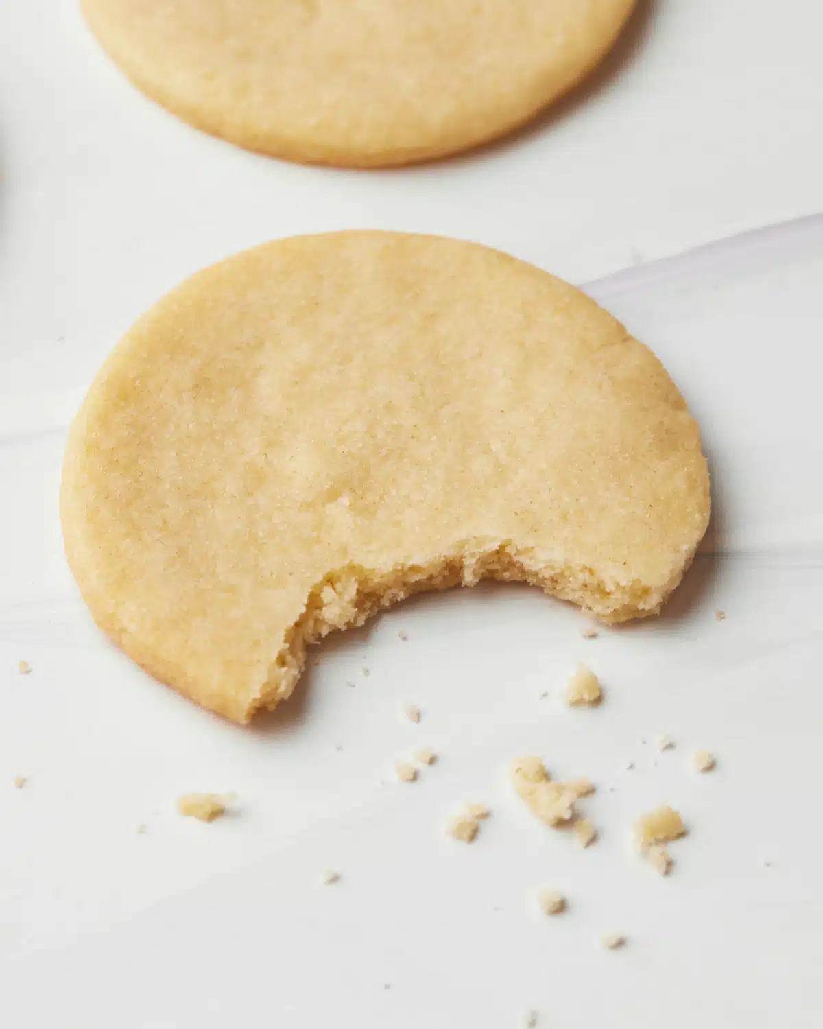 Sugar cookie with a bite taken out of it and crumbs next to it.